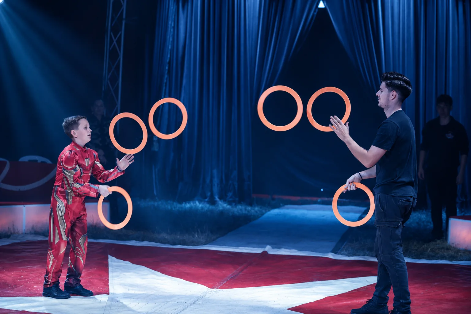 Zwei Jongleure spielen sich leuchtende Ringe in der Manege zu